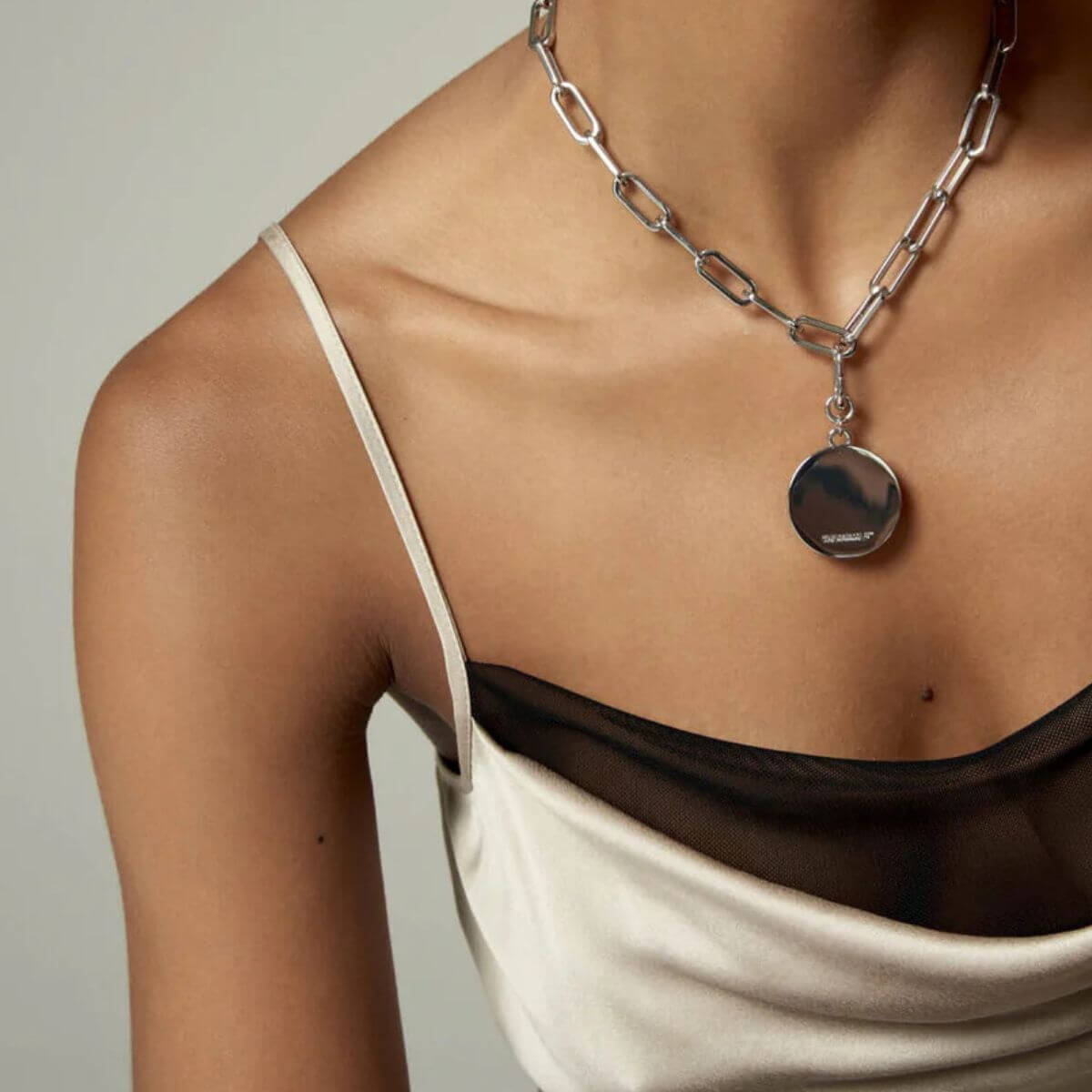 The Animals necklace with large silver disc pendant styled on a woman wearing a satin and mesh dress. Die The Animals Halskette mit großem silbernen Anhänger, getragen von einer Frau im Satin- und Meshkleid. Collier The Animals avec un grand pendentif rond en argent porté par une femme en robe satinée et transparente.