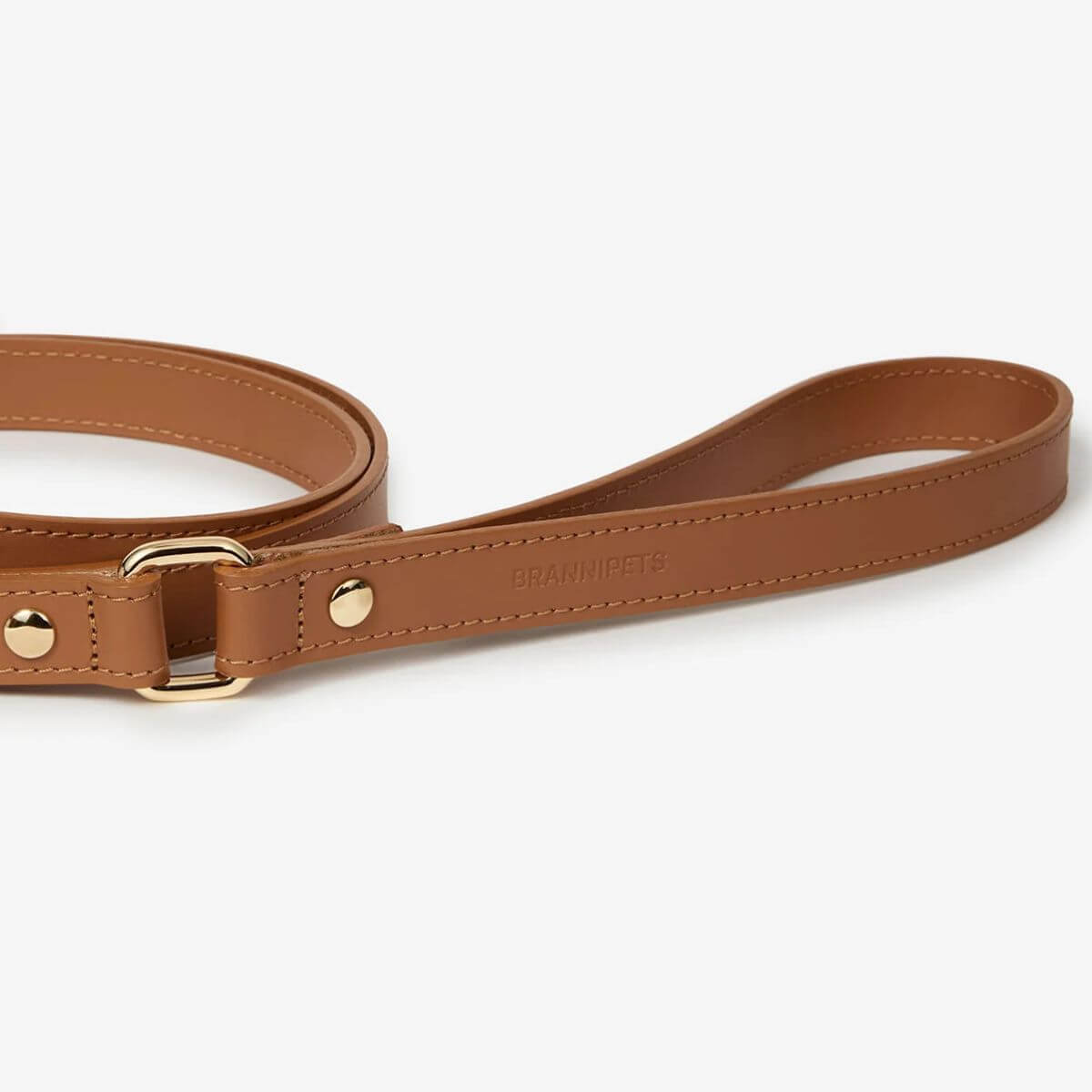 Detail of the Branni Pets caramel brown dog leash handle with visible logo engraving and elegant gold buckle. Detailansicht des Griffes der karamellbraunen Hundeleine von Branni Pets mit sichtbarem Logo und eleganter goldener Schnalle. Détail de la poignée de la laisse pour chien Branni Pets en caramel avec logo visible et boucle dorée élégante.