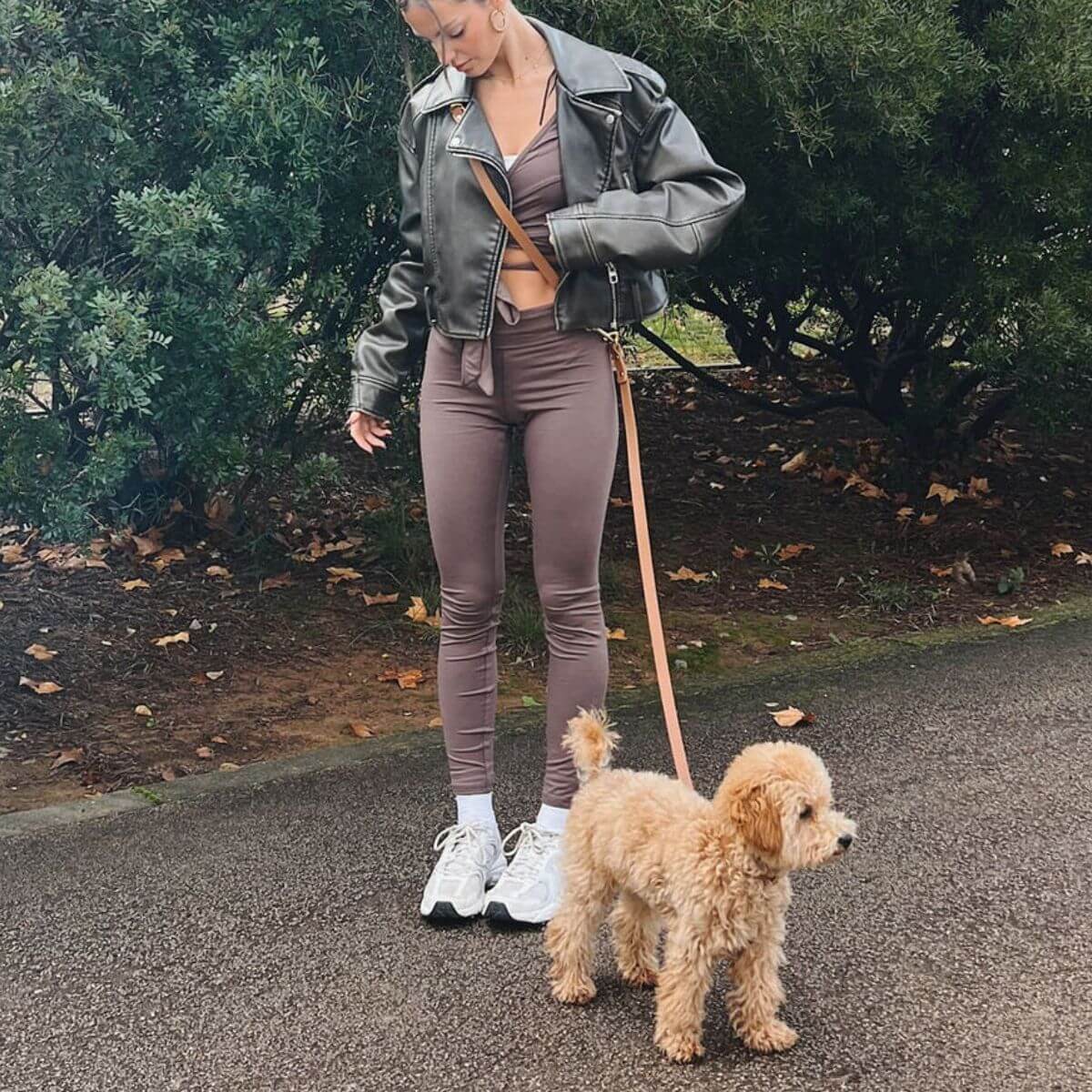 Lifestyle image showing the caramel brown Branni Pets dog leash during a walk, styled with activewear and a leather jacket for a casual, elegant look. Lifestyle-Bild der karamellbraunen Hundeleine von Branni Pets beim Spaziergang, kombiniert mit Sportkleidung und Lederjacke für einen lässig-eleganten Look. Image lifestyle de la laisse Branni Pets caramel portée lors d’une promenade, assortie à une tenue décontractée avec veste en cuir.