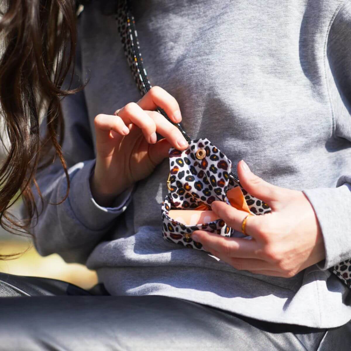 Close-up of a person opening the French Bandit leopard print poop bag holder – practical and stylish for everyday walks. Nahaufnahme einer Person beim Öffnen des French Bandit Kotbeutelhalters im Leopardenmuster – praktisch und stilvoll für den Alltag. Gros plan d’une personne ouvrant le distributeur de sacs à imprimé léopard de French Bandit – pratique et élégant pour les promenades quotidiennes.