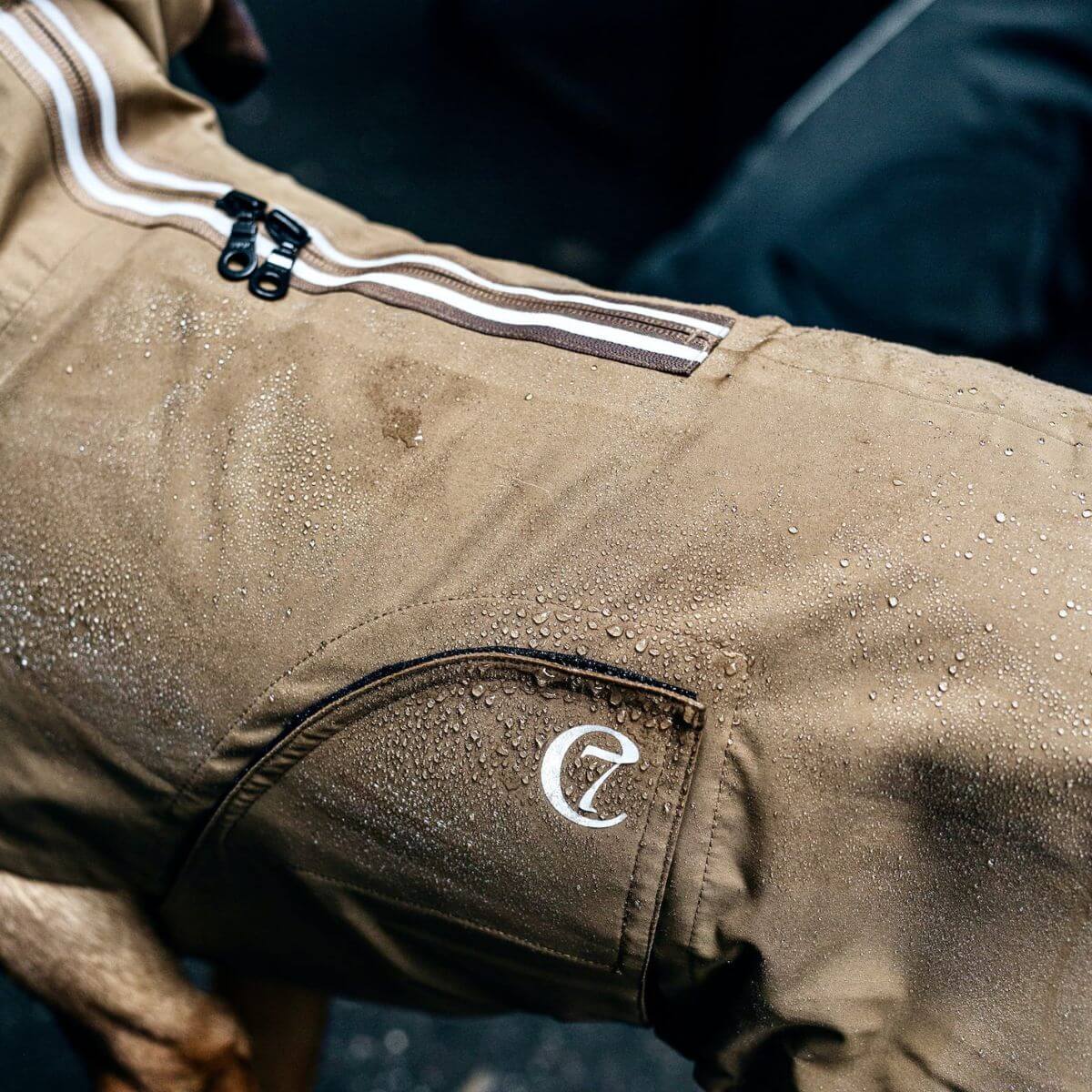 Water droplets on waterproof tan Cloud7 dog raincoat with logo patch.
Wassertropfen auf wasserdichtem, beigen Cloud7 Hunderegenmantel mit Logopatch.
Gouttes d’eau sur l’imperméable beige imperméable pour chien Cloud7 avec logo.