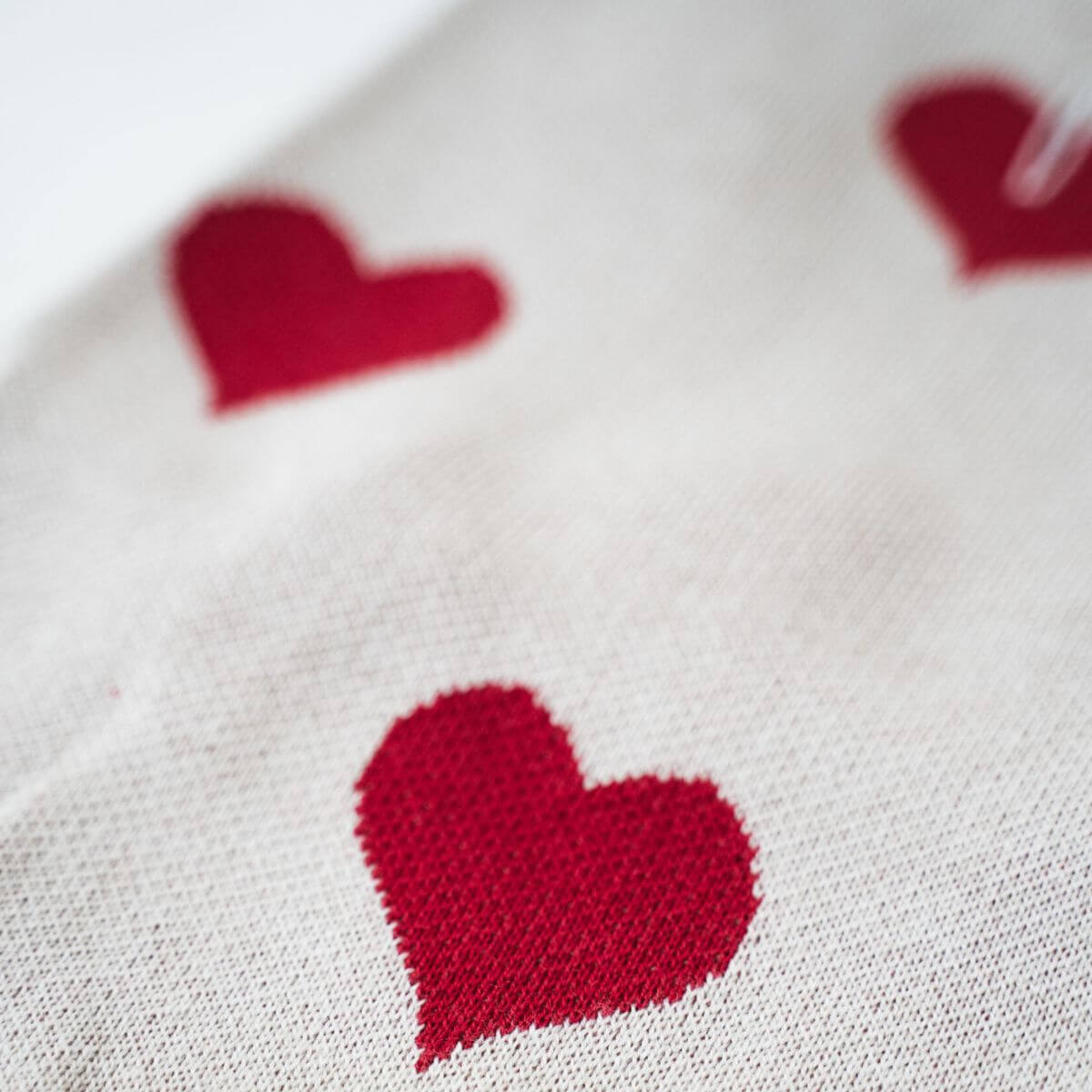 Close-up of knitted red hearts on cream dog sweater by Lou and Co. Nahaufnahme des Strickpullovers mit roten Herzen von Lou and Co. Gros plan sur les cœurs rouges tricotés sur le pull crème de Lou and Co.