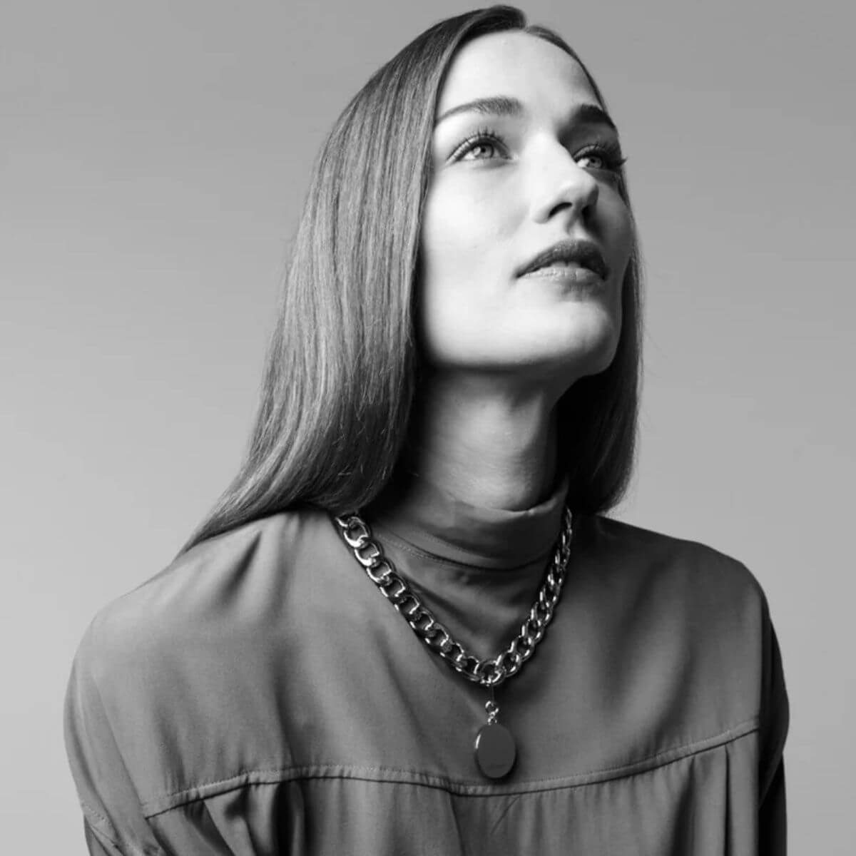 The Animals curb chain necklace with round silver pendant, worn by a woman in a monochrome portrait.
Halskette mit silbernem Anhänger von The Animals, getragen von einer Frau im monochromen Porträt.
Collier à maillons avec pendentif rond argenté de The Animals, porté par une femme dans un portrait en noir et blanc.