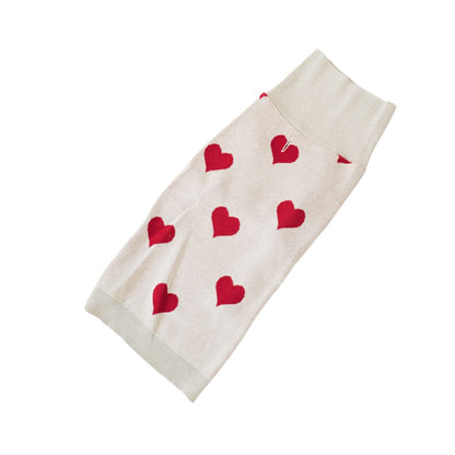 Overhead shot of a beige dog sweater with red hearts.