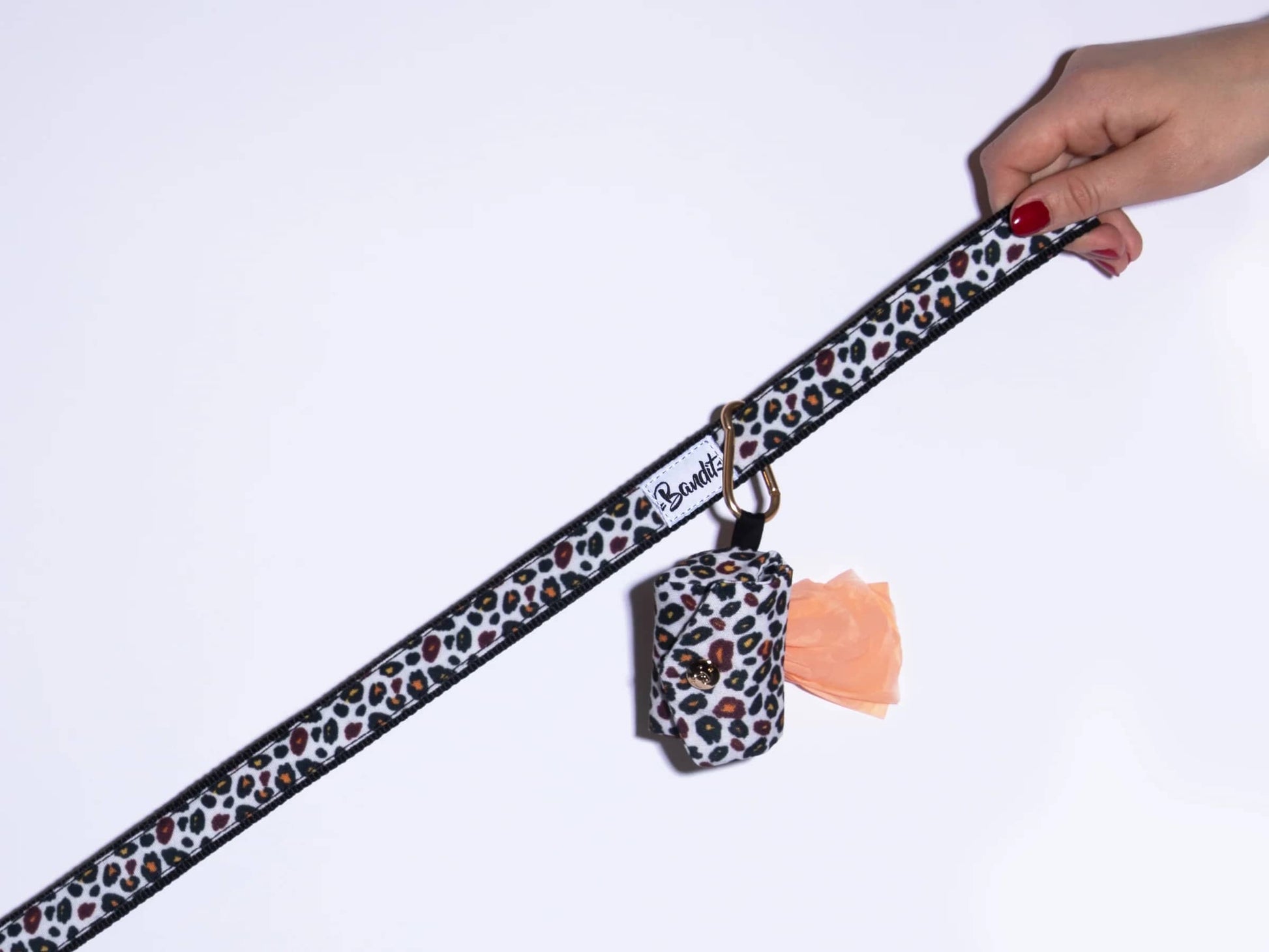 Hand holding a leopard printed dog poop bag holder with gold hardware by French Bandit