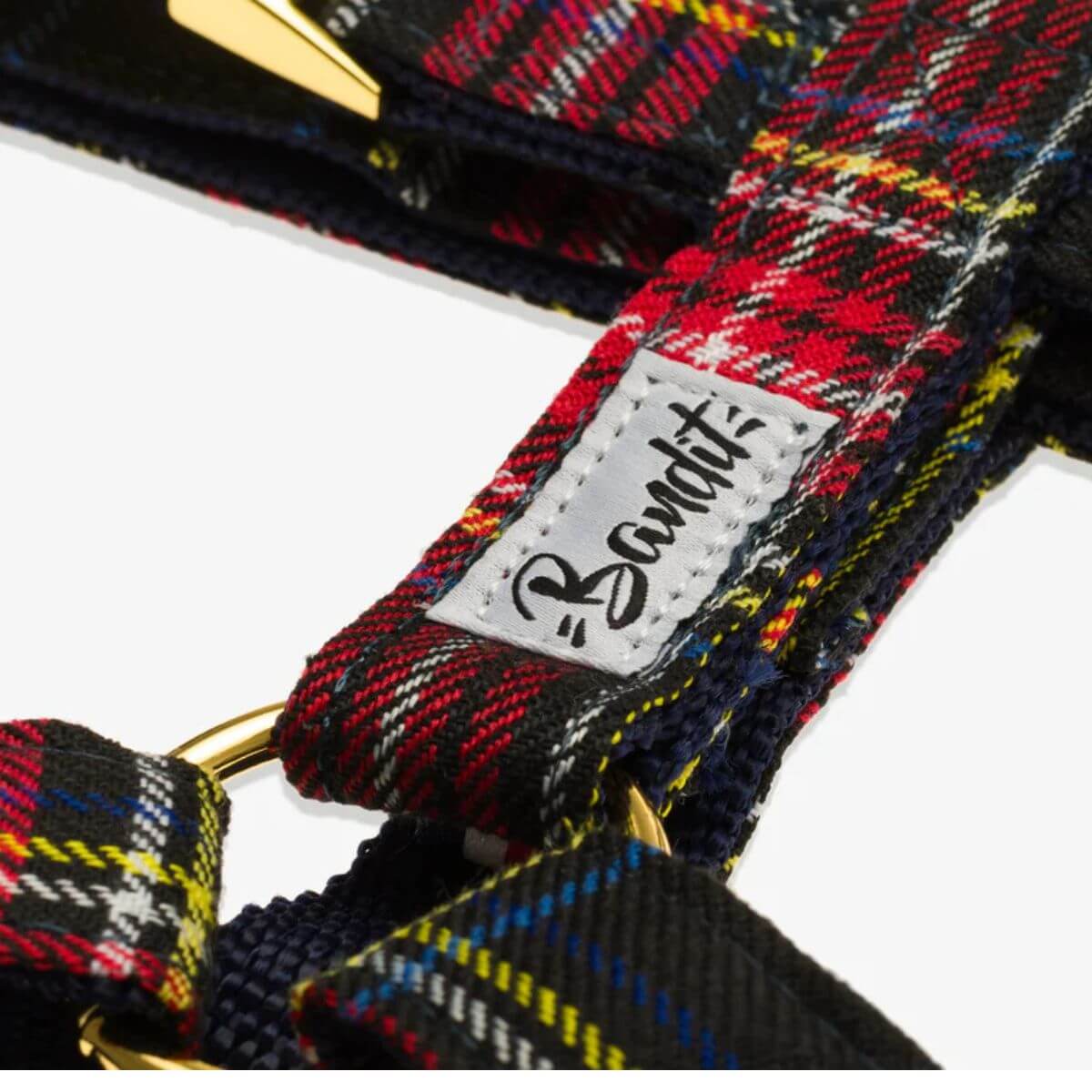 Close-up of the French Bandit dog harness in red tartan with gold ring and stitched brand label – high-quality detail and design. Detailaufnahme des French Bandit Hundegeschirrs im roten Tartan-Muster mit goldfarbenem Ring und genähtem Markenetikett – hochwertiges Design. Gros plan du harnais pour chien French Bandit en tartan rouge avec anneau doré et étiquette cousue – design de haute qualité.