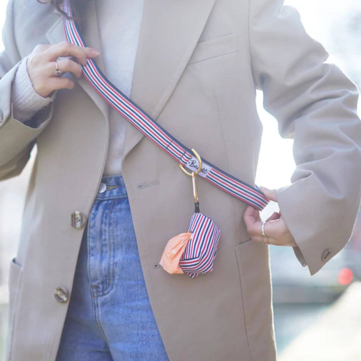 Person wearing a French Bandit red, white, and blue striped leash crossbody with attached poop bag holder – stylish and hands-free dog walking solution. Person trägt French Bandit Hundeleine in Rot-Weiß-Blau als Crossbody mit angehängtem Kotbeutelhalter – modische freihändige Gassi-Lösung. Personne portant une laisse rayée rouge, blanche et bleue de French Bandit en bandoulière avec distributeur de sacs attaché – solution élégante et mains libres.