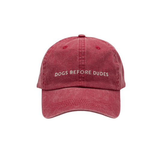 Front view of washed red denim baseball cap with "DOGS BEFORE DUDES" embroidery by Collar of Sweden. Vorderansicht der verwaschenen roten Denim-Basecap mit "DOGS BEFORE DUDES"-Stickerei von Collar of Sweden. Vue de face de la casquette en denim rouge délavé avec broderie "DOGS BEFORE DUDES" de Collar of Sweden.
