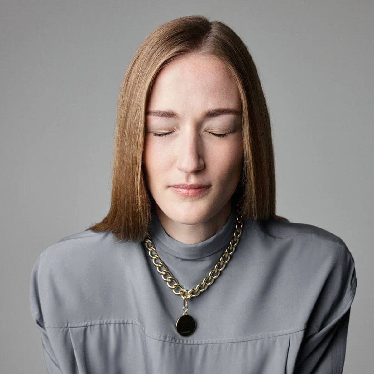 The Animals woman wearing chunky gold curb chain necklace with round pendant, eyes closed in soft light.
Frau trägt goldene The Animals Panzerkette mit rundem Anhänger, Augen geschlossen, weiches Licht.
Femme portant le collier gourmette doré The Animals avec pendentif rond, yeux fermés, lumière douce.