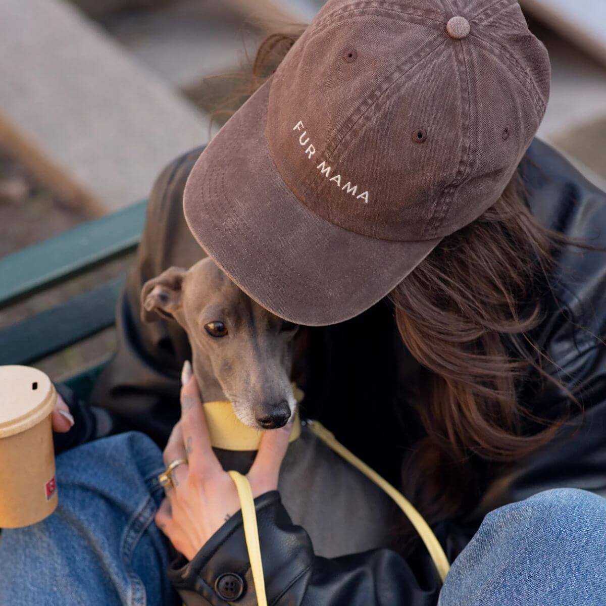 'Fur Mama' cap by Collar of Sweden worn by a woman cuddling her dog on a bench / Casquette 'Fur Mama' de Collar of Sweden portée par une femme câlinant son chien sur un banc / 'Fur Mama' Kappe von Collar of Sweden getragen von einer Frau, die ihren Hund auf einer Bank hält