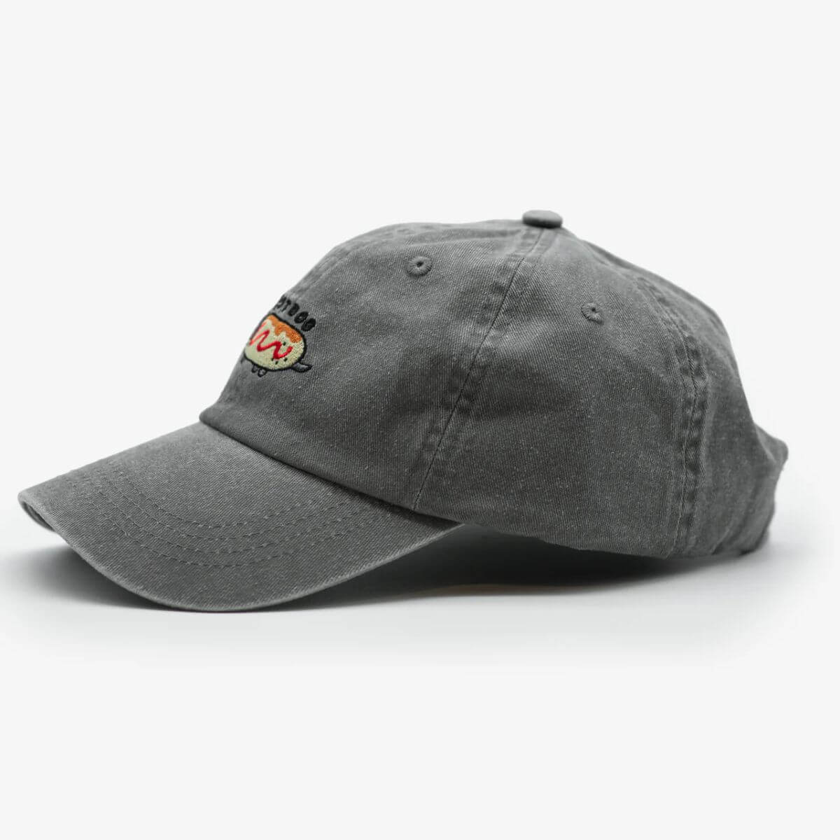 Side view of the washed grey denim “Hot Dog” cap with Dachshund embroidery by Collar of Sweden – for dachshund lovers and owners – Vue latérale de la casquette en denim gris délavé “Hot Dog” avec broderie teckel de Collar of Sweden – pour les amoureux et propriétaires de teckels – Seitenansicht der grauen, gewaschenen “Hot Dog”-Kappe mit Dackel-Stickerei von Collar of Sweden – für Dackelliebhaber und -besitzer.