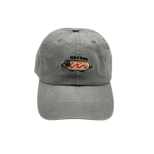 Front view of washed grey denim “Hot Dog” cap by Collar of Sweden, featuring embroidered Dachshund in a hot dog bun – perfect for dachshund lovers and owners – Vue de face de la casquette en denim gris délavé “Hot Dog” de Collar of Sweden, avec un teckel brodé en pain hot-dog – parfaite pour les amoureux et propriétaires de teckels – Vorderansicht der grauen, gewaschenen “Hot Dog”-Kappe von Collar of Sweden mit gesticktem Dackel im Hotdog-Brötchen – perfekt für Dackelfreunde und -besitzer.